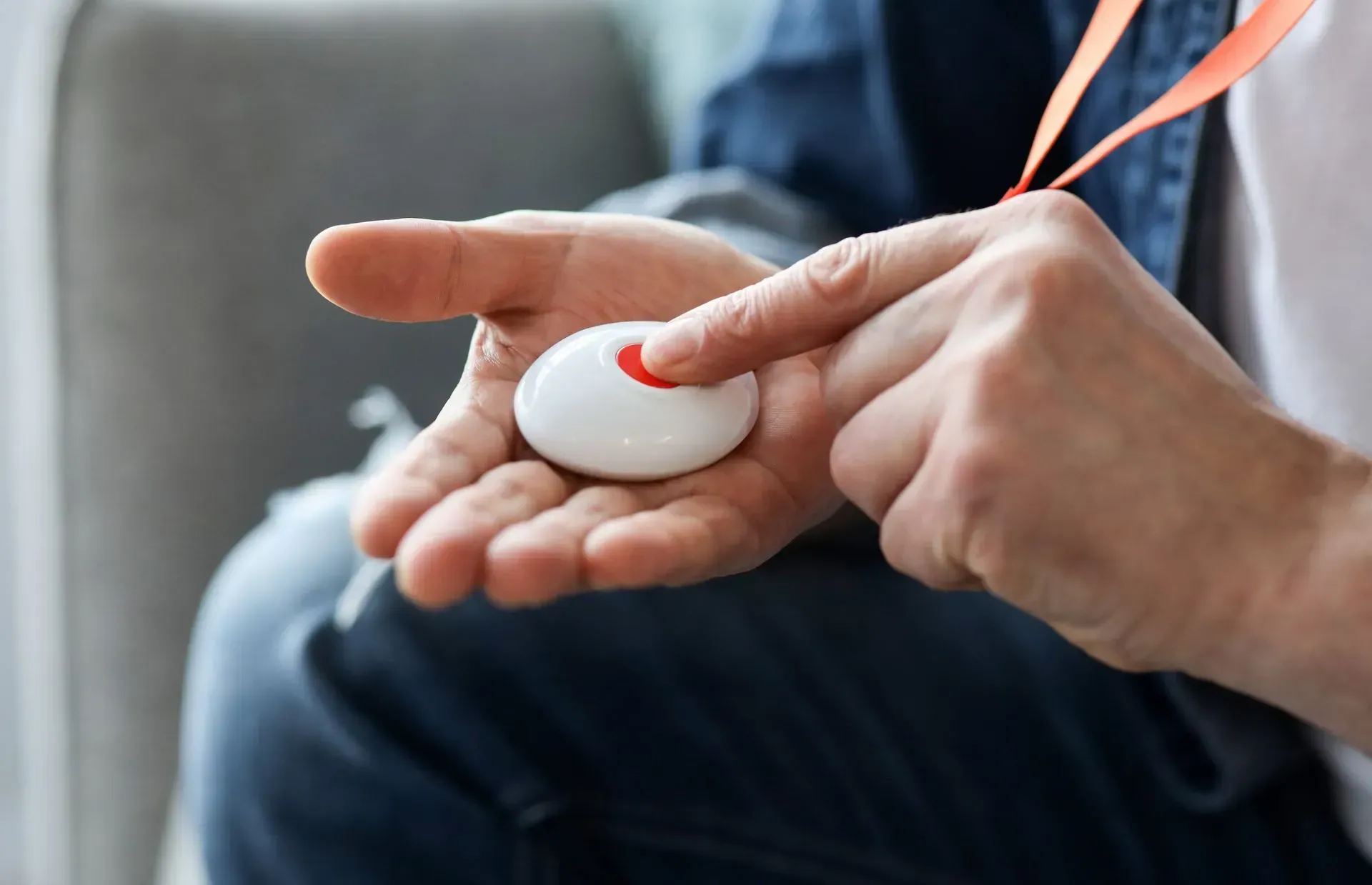 Une personne appuie sur le bouton rouge d'un dispositif d'alerte d'urgence portable blanc qu'elle tient dans la paume de sa main.