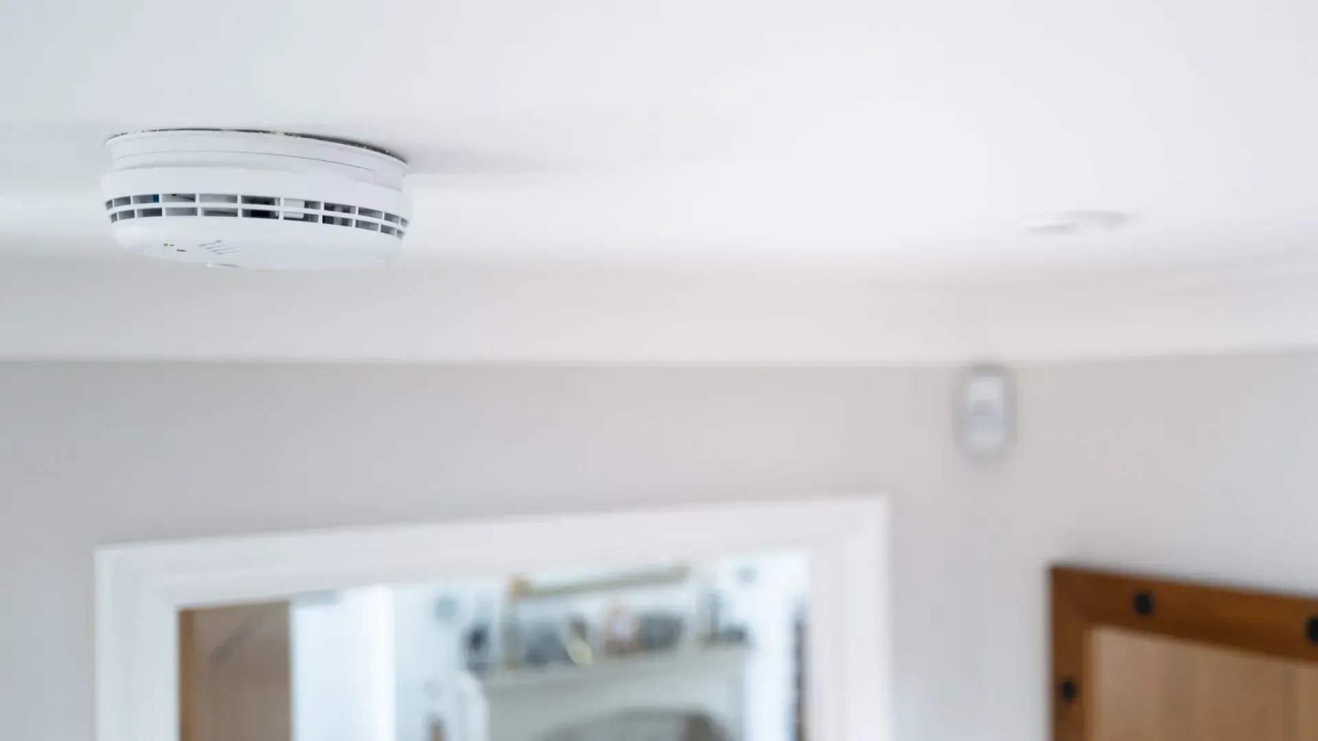Un détecteur de fumée blanc est fixé au plafond blanc, au-dessus d'un coin de la pièce.
