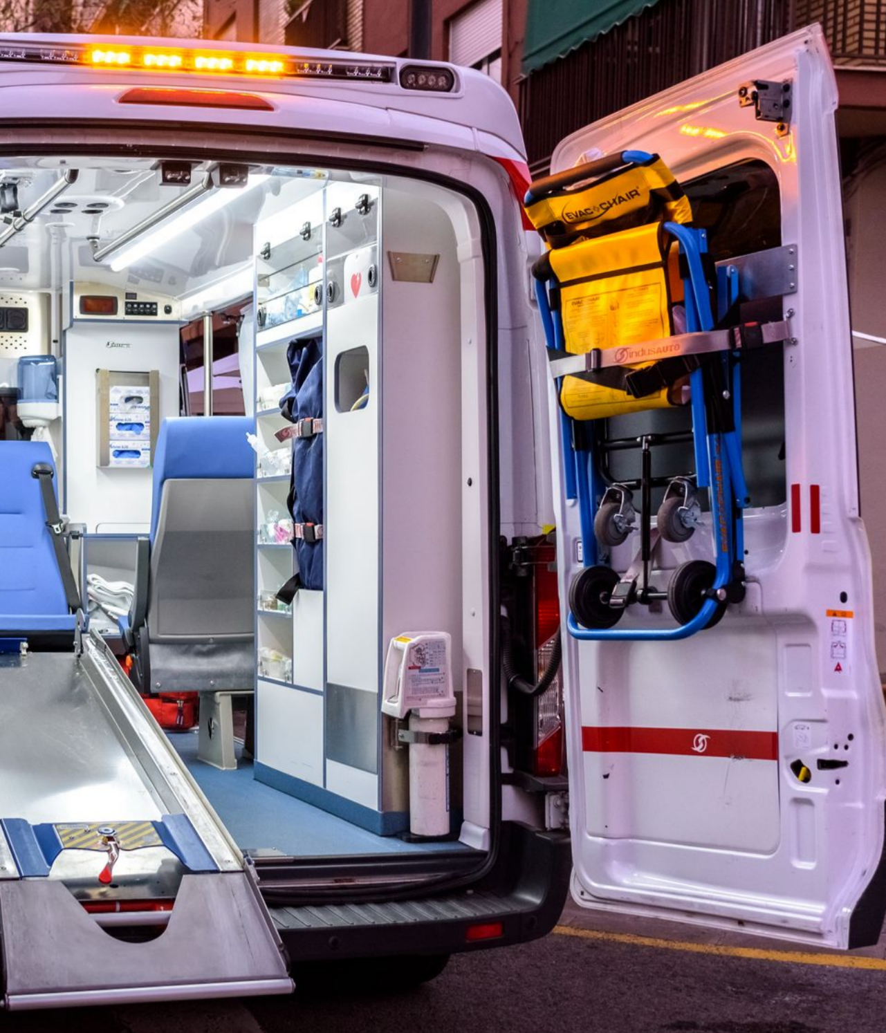 Intérieur d'une ambulance avec équipement médical. Un brancard est fixé à la porte, des armoires et des sièges sont visibles.