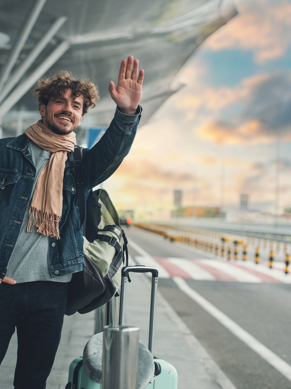 Un homme faisant signe de la main, debout près des bagages à l'aéroport ; coucher de soleil.