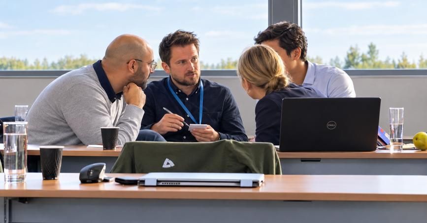 Teambesprechung an einem weissen Tisch mit Laptops, Tablets, Kaffeetassen und Diagrammen aus der Vogelperspektive.