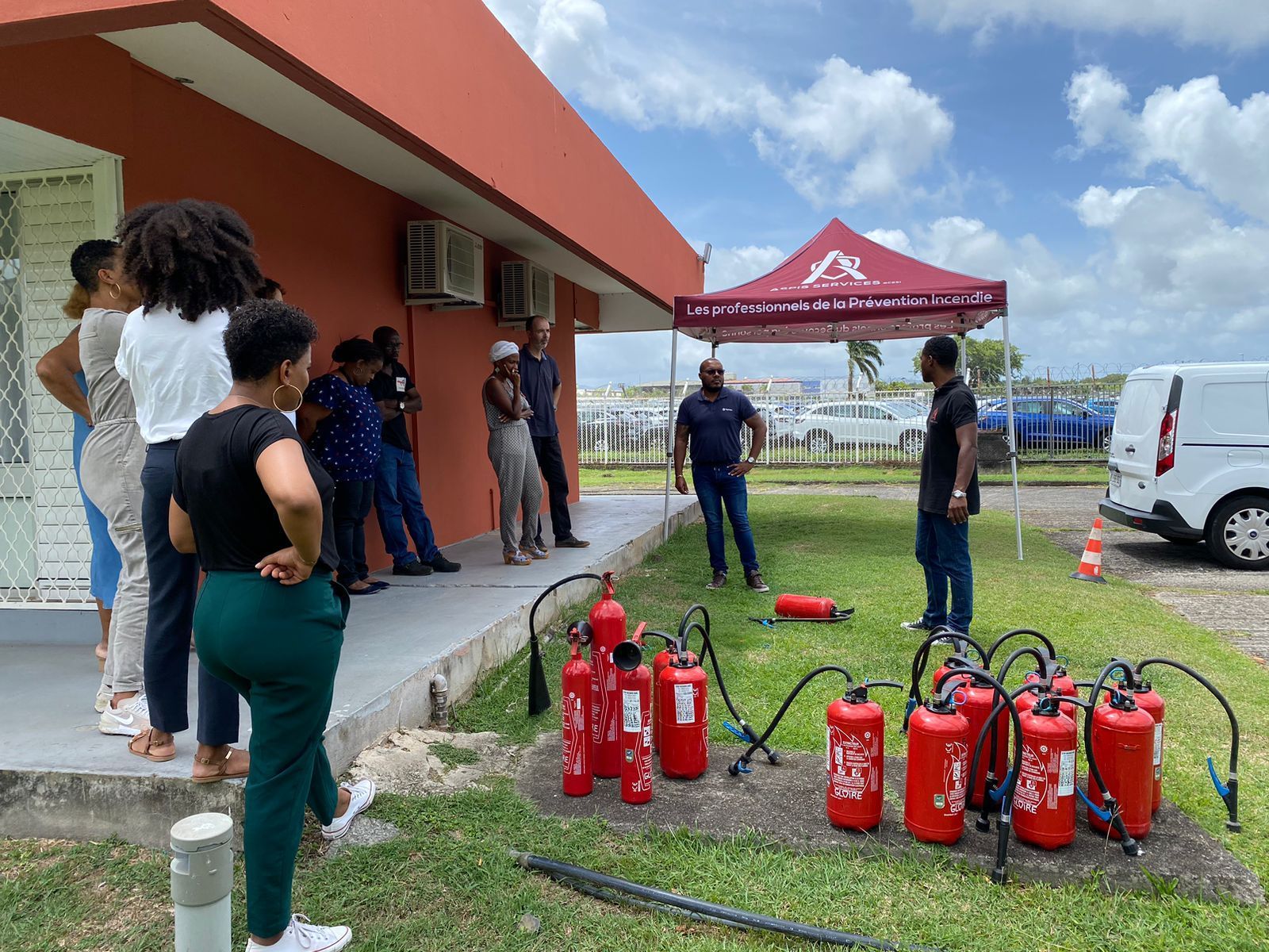 Deux formateurs encadrent un groupe en formation sécurité incendie à l’extérieur, avec des extincteurs posés au sol