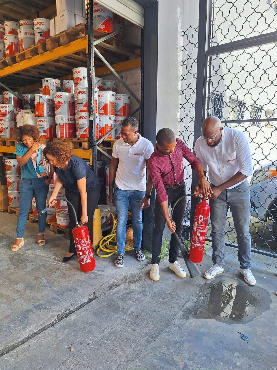 Participants manipulant des extincteurs lors d'une démonstration de sécurité incendie en entrepôt.