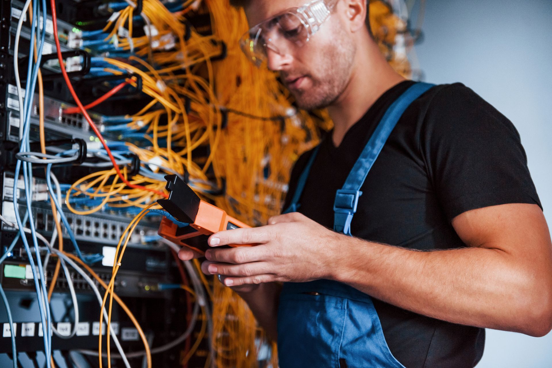 Un técnico con gafas de seguridad examina los cables en la sala de servidores utilizando un multímetro.