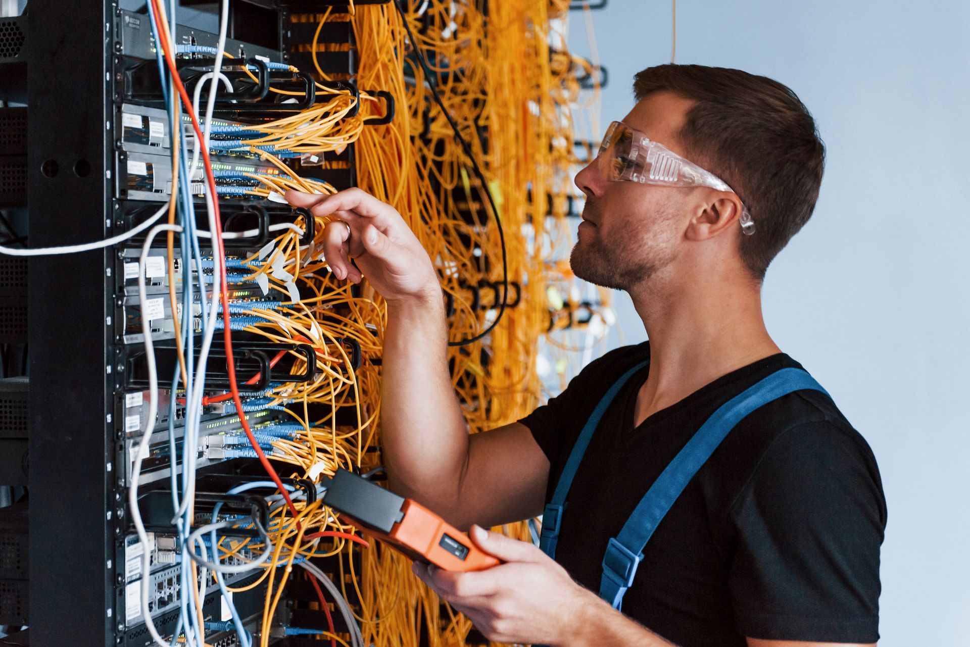 Hombre con gafas de seguridad trabajando en un rack de servidores, rodeado de cables y alambres.