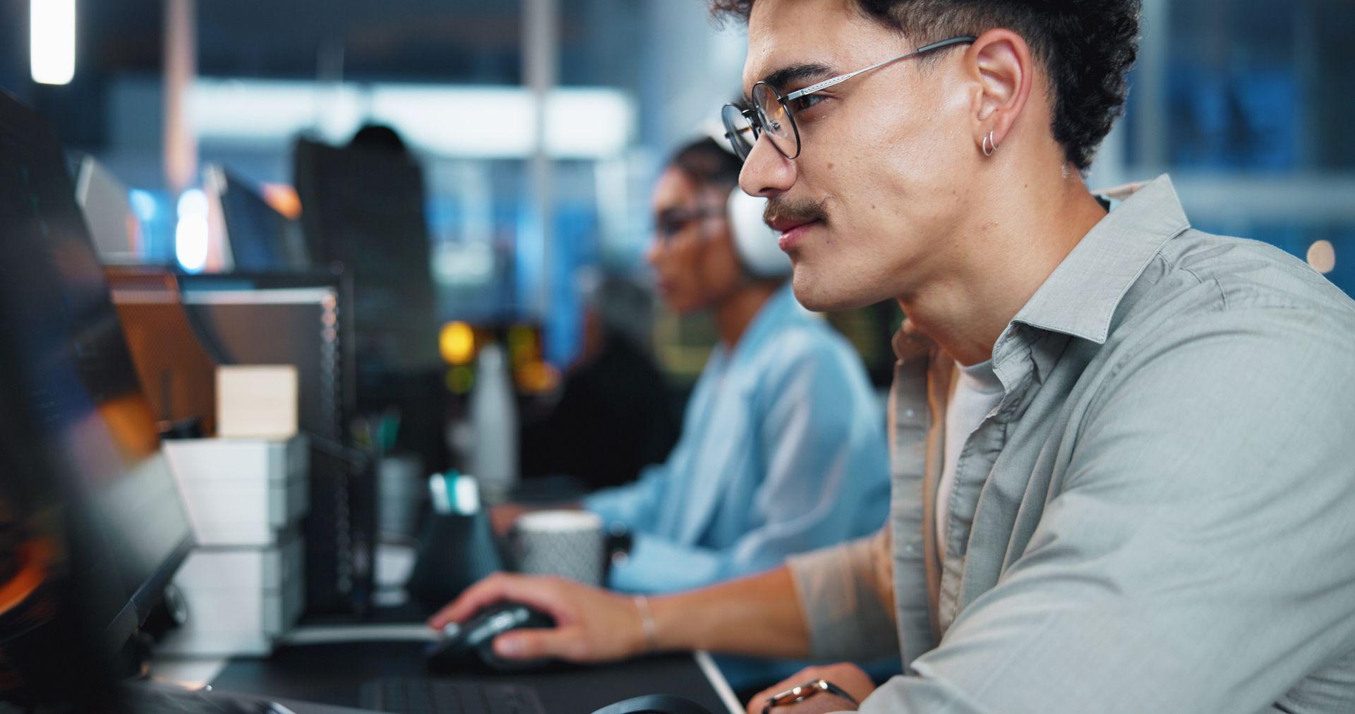Hombre con gafas y bigote trabajando en una computadora, en un entorno de oficina.
