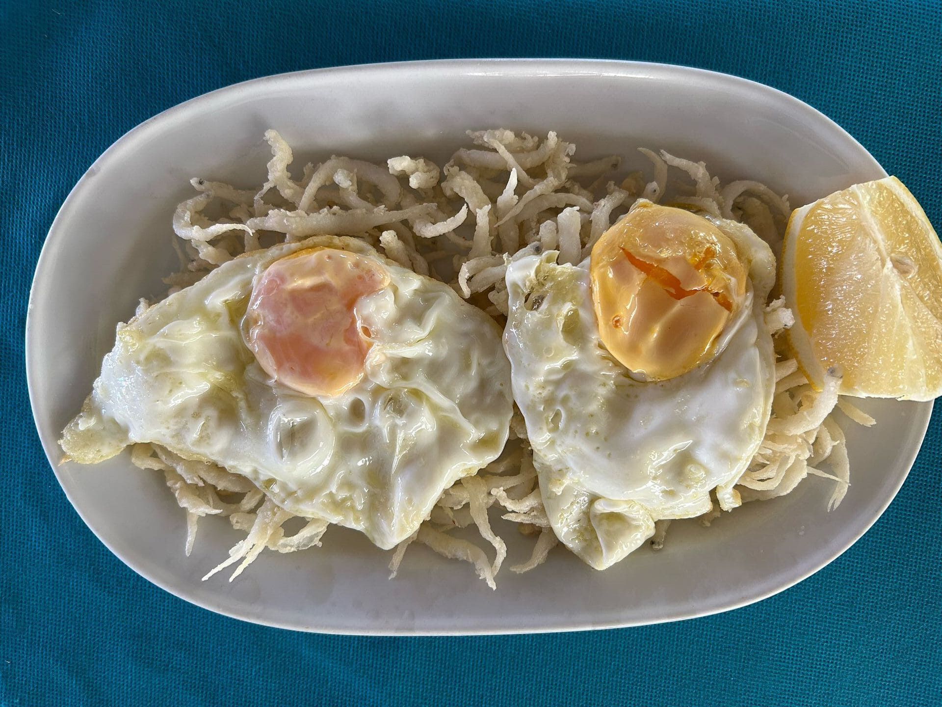 Un plato blanco cubierto con huevos fritos y fideos con una rodaja de limón.