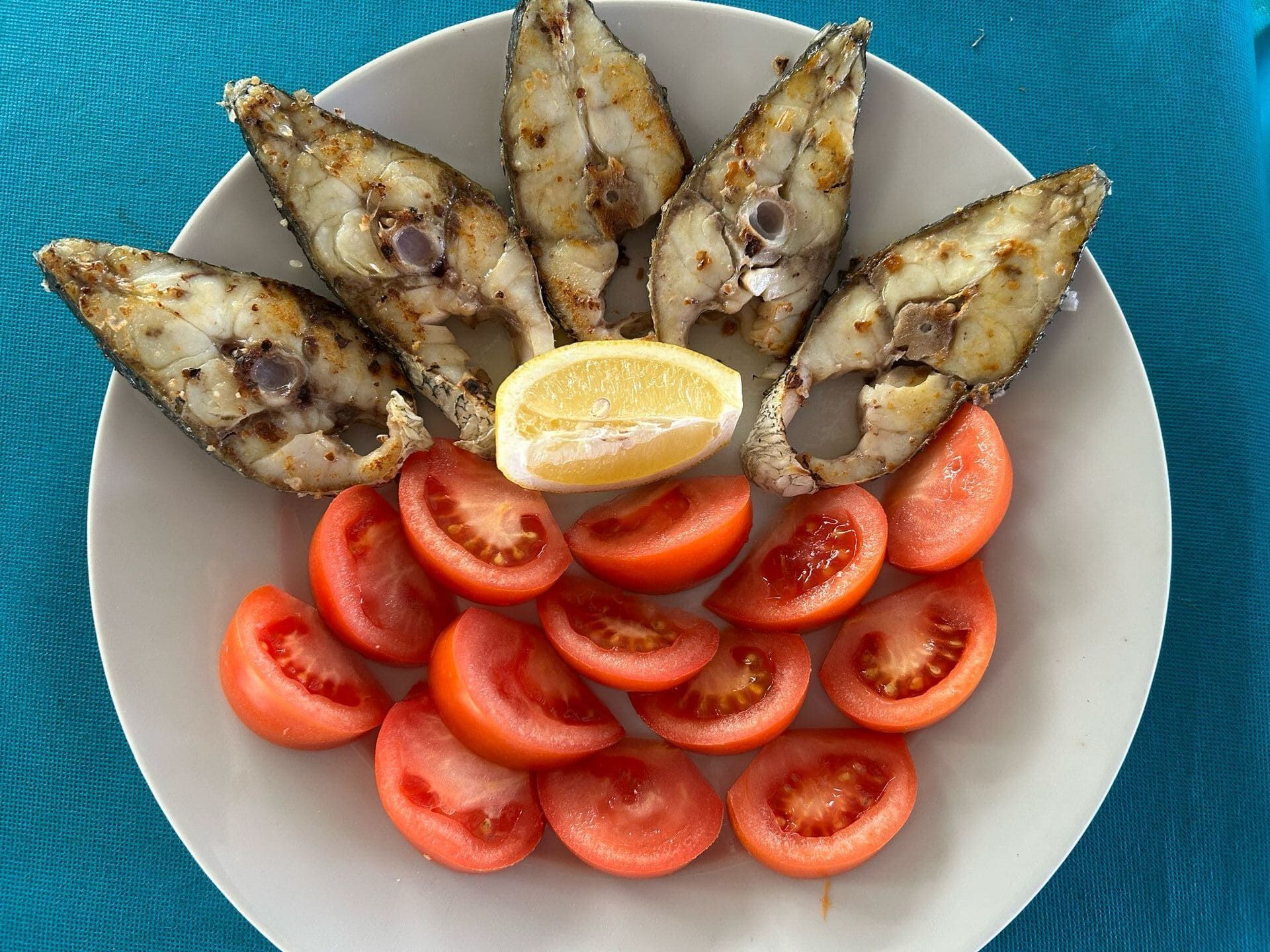 Un plato de pescado y tomates con una rodaja de limón encima.