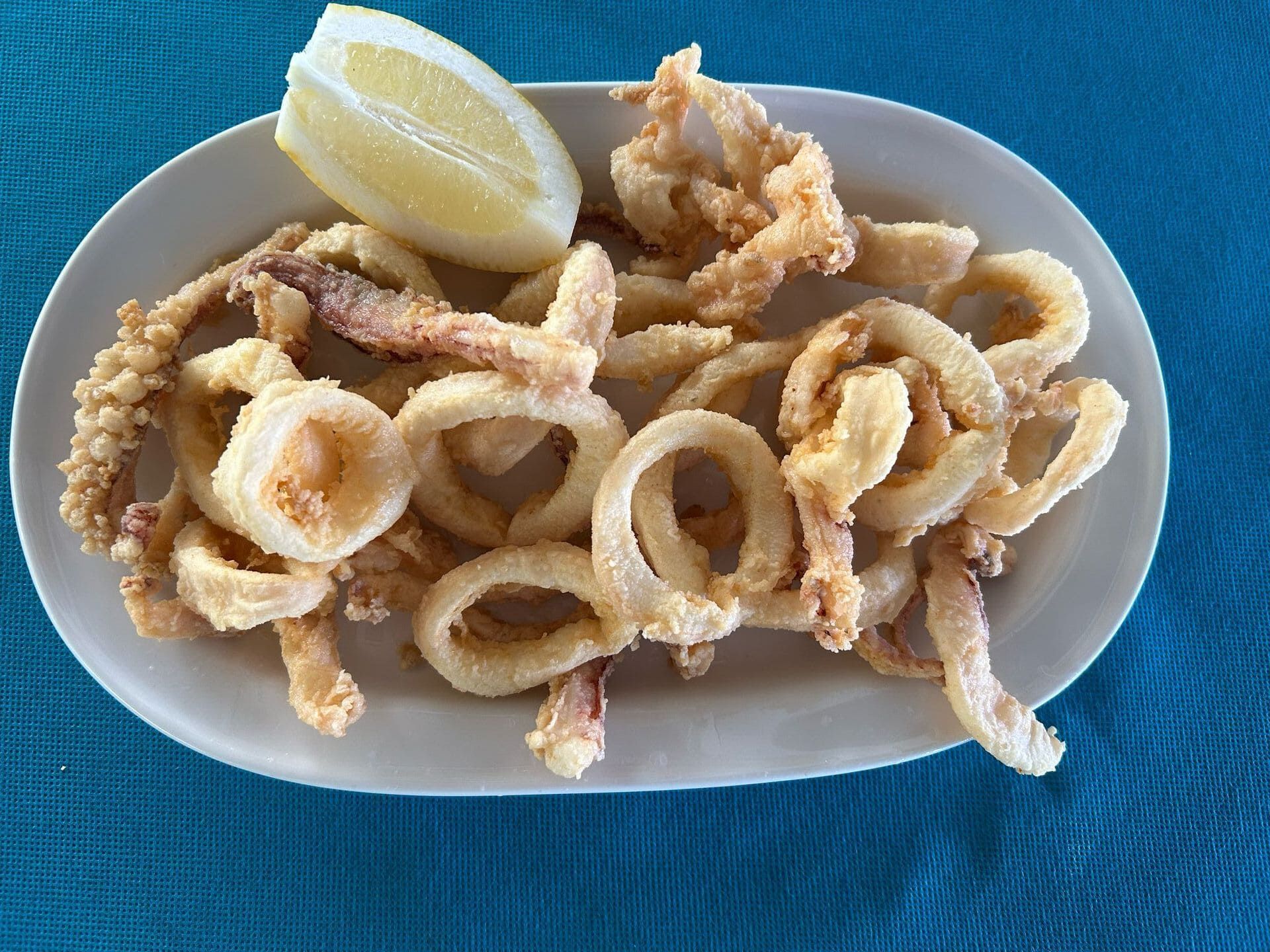Un plato de calamares fritos con una rodaja de limón sobre una mesa.