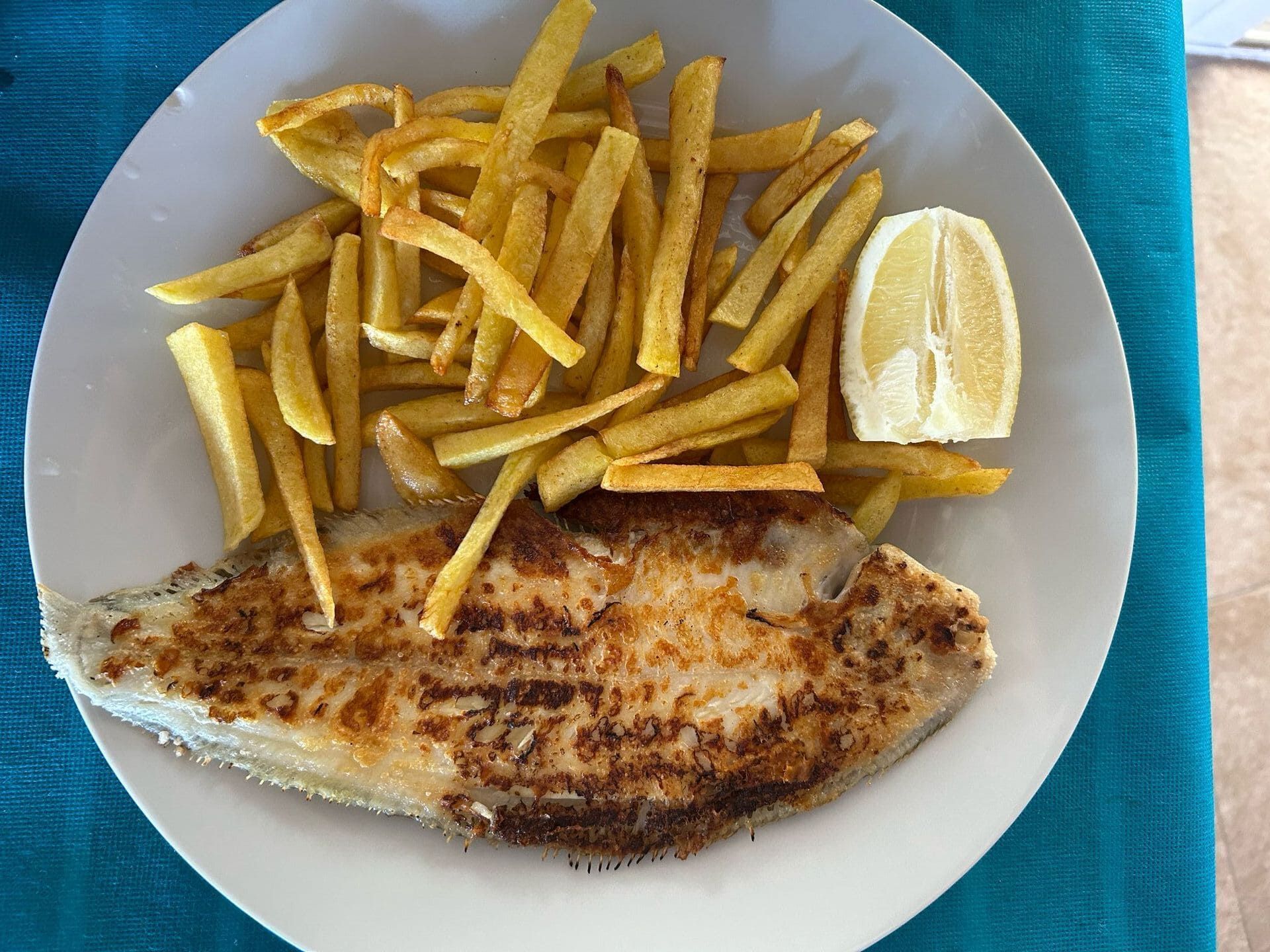 Un plato blanco cubierto con pescado y papas fritas.