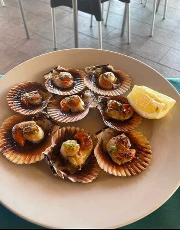 Un plato blanco cubierto con vieiras y una rodaja de limón.