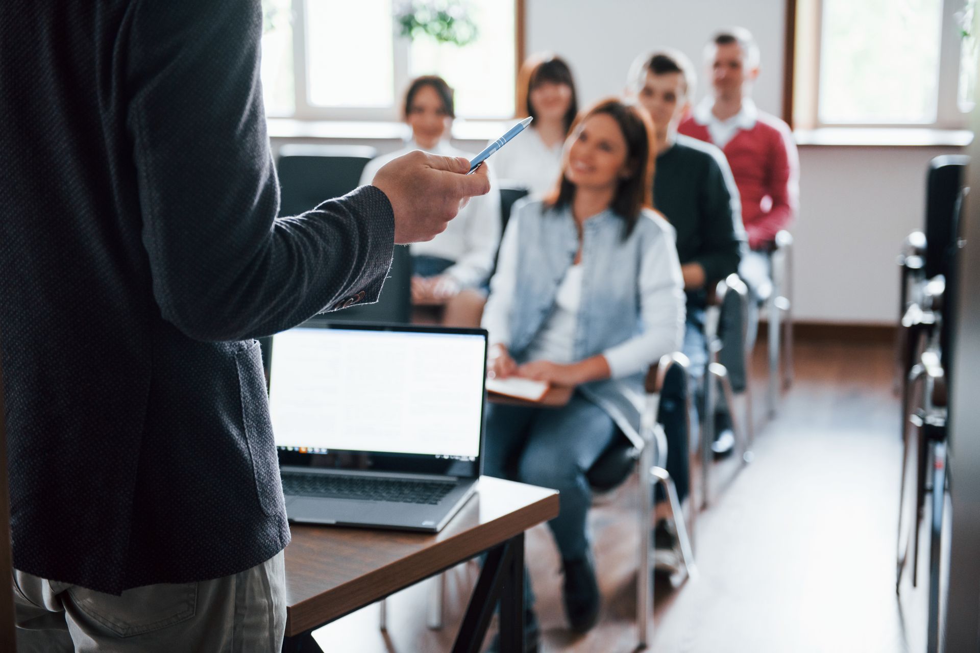 Un instructor con un bolígrafo se dirige a un grupo de estudiantes sentados en un salón de clases.