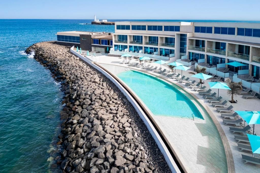 Resort à beira-mar com piscina, espreguiçadeiras e prédio com detalhes em azul.