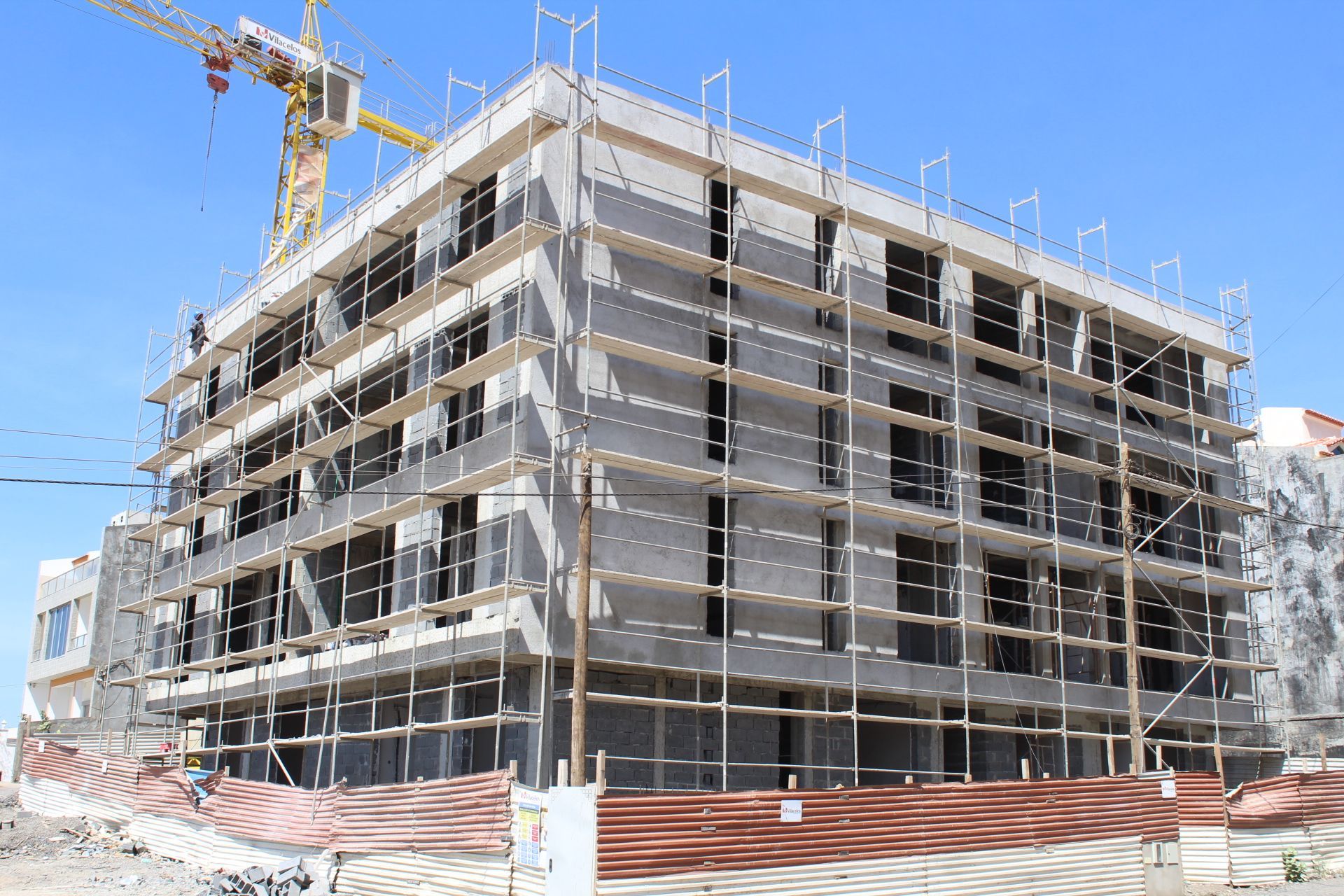 Prédio em construção com andaimes e guindaste em um dia ensolarado.