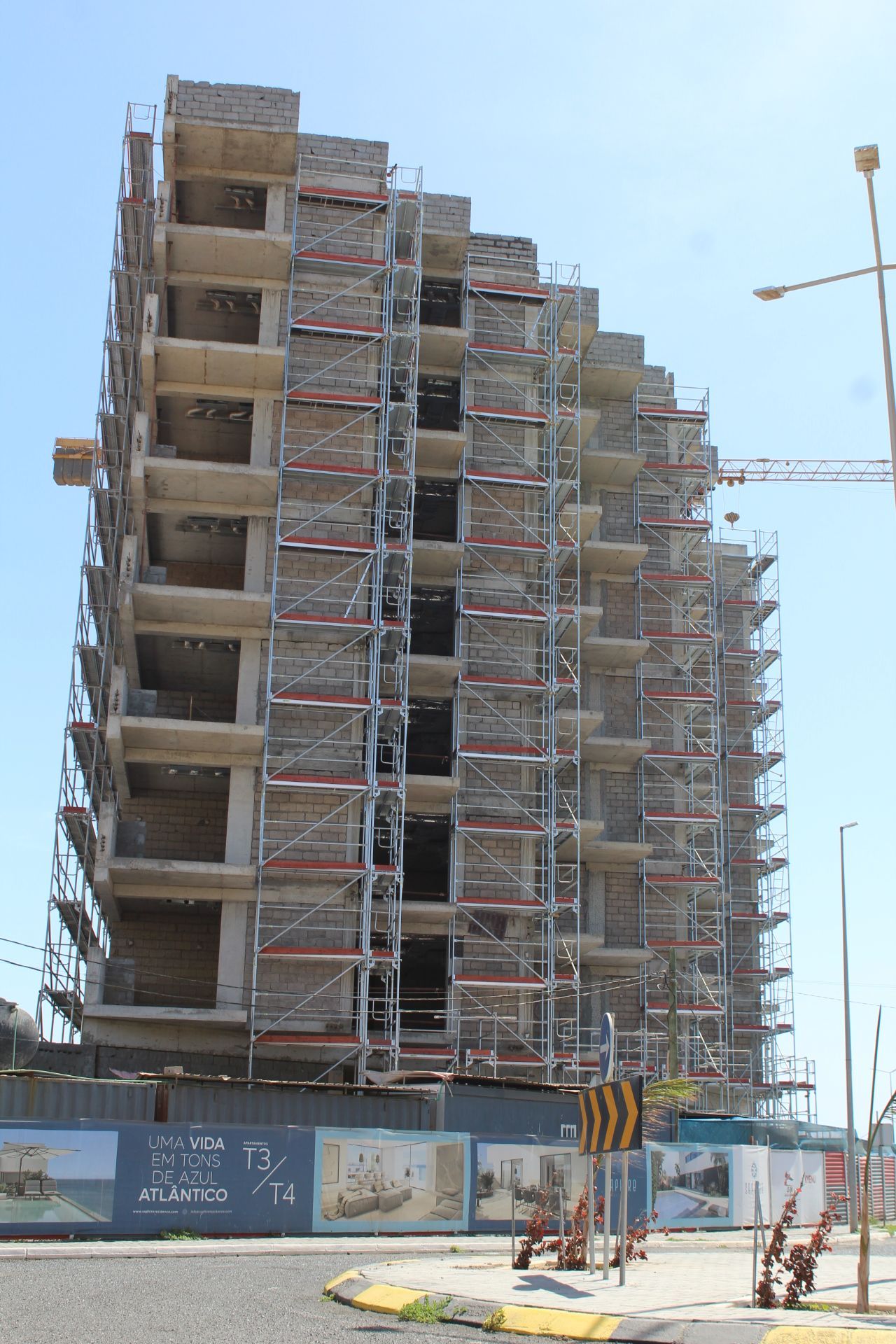 Um prédio de vários andares em construção, com andaimes e um guindaste, em um dia ensolarado.
