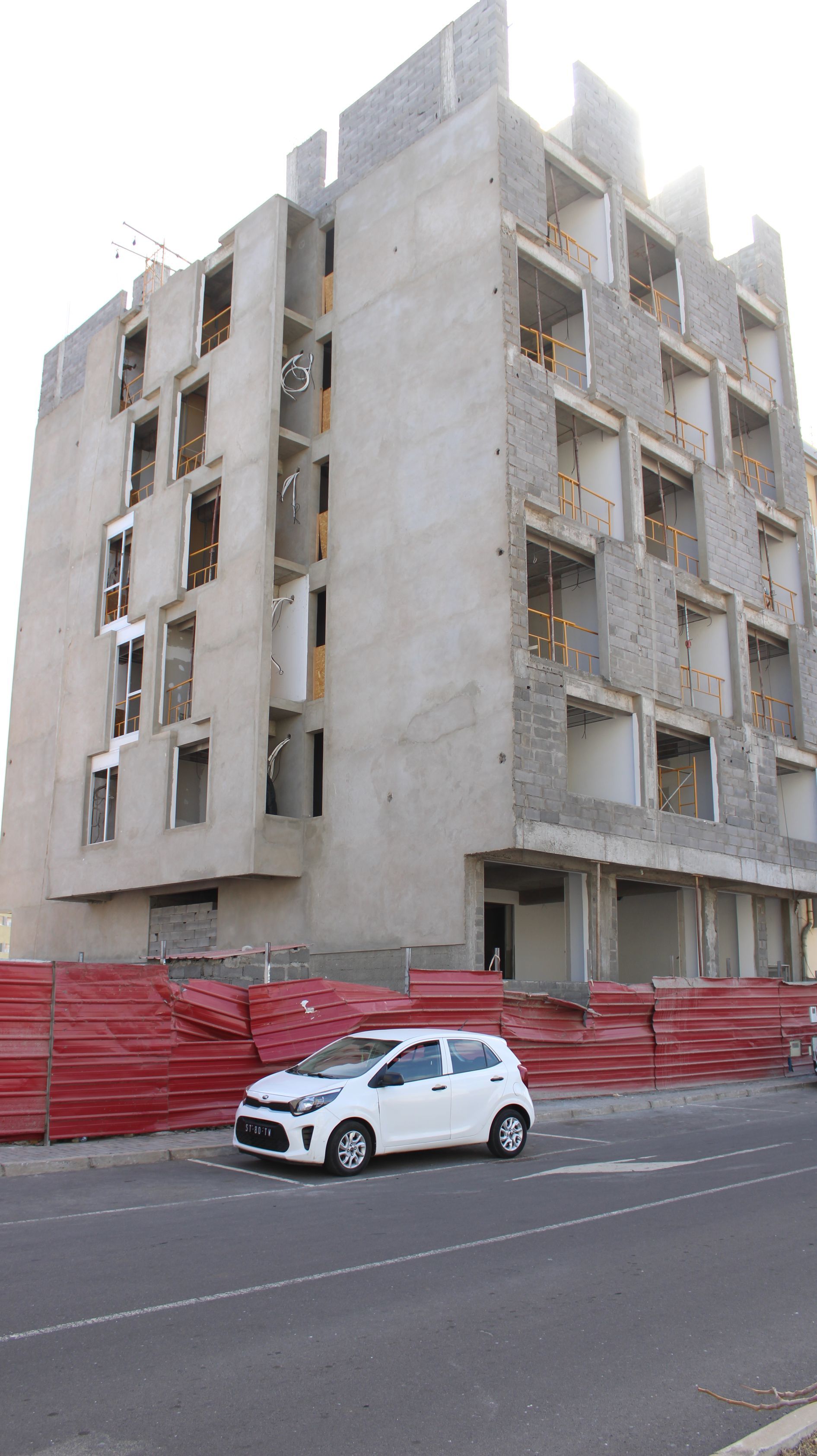 Prédio em construção com um carro branco estacionado em frente.