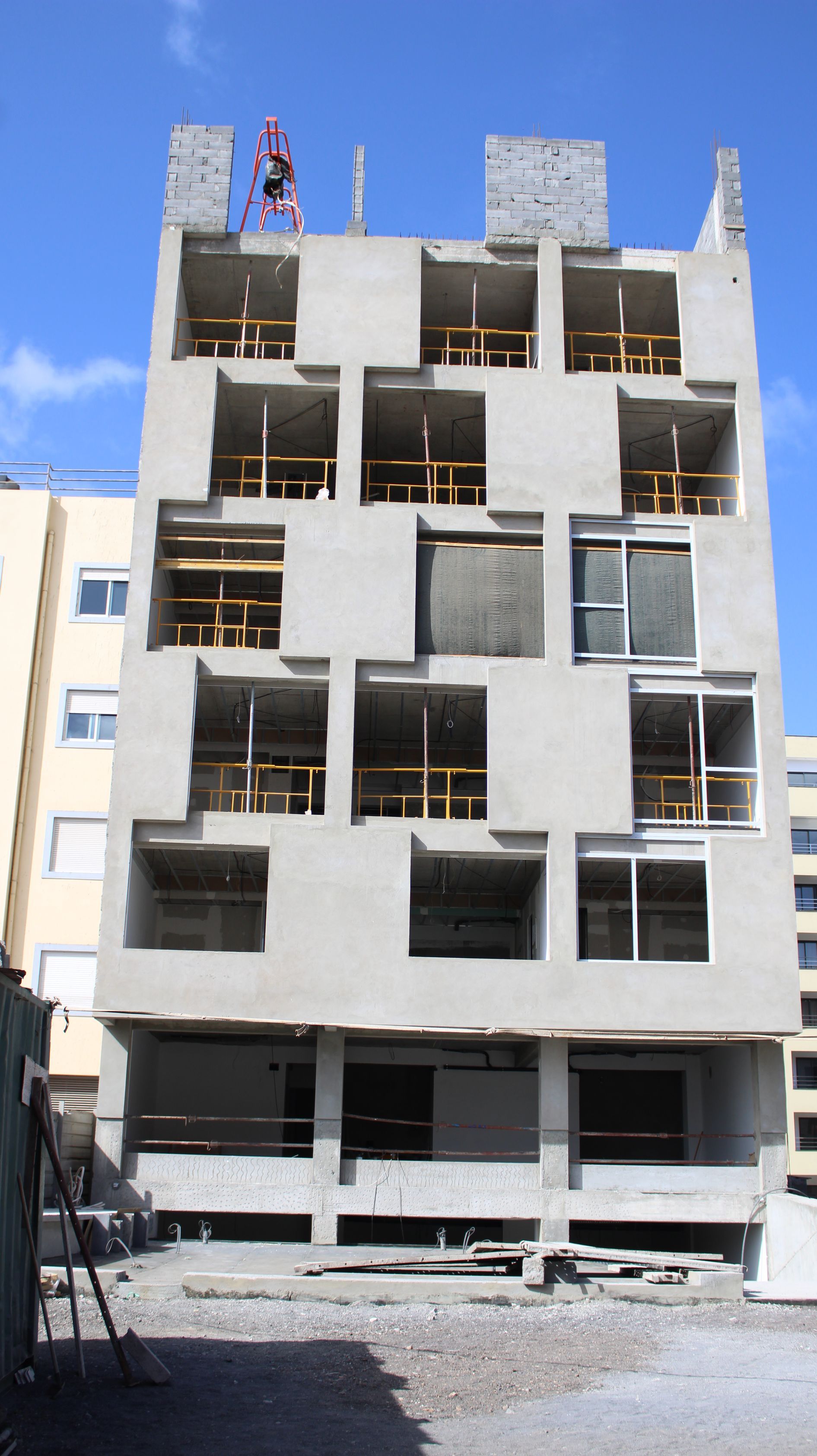 Prédio de concreto inacabado com janelas quadradas; vigas de sustentação de madeira visíveis.