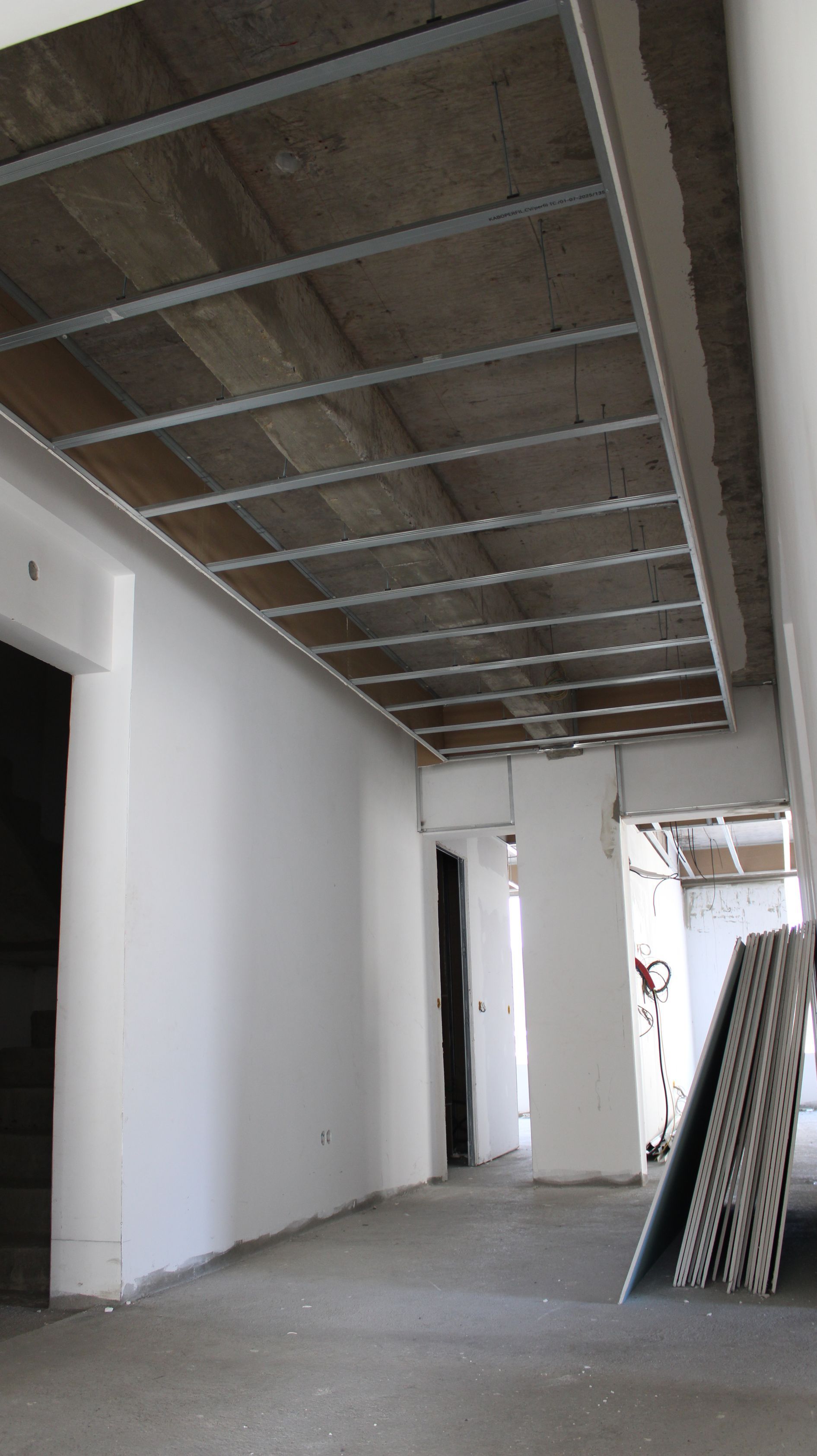 Interior de uma obra. Estrutura do teto aparente, painéis de concreto, paredes brancas, porta,