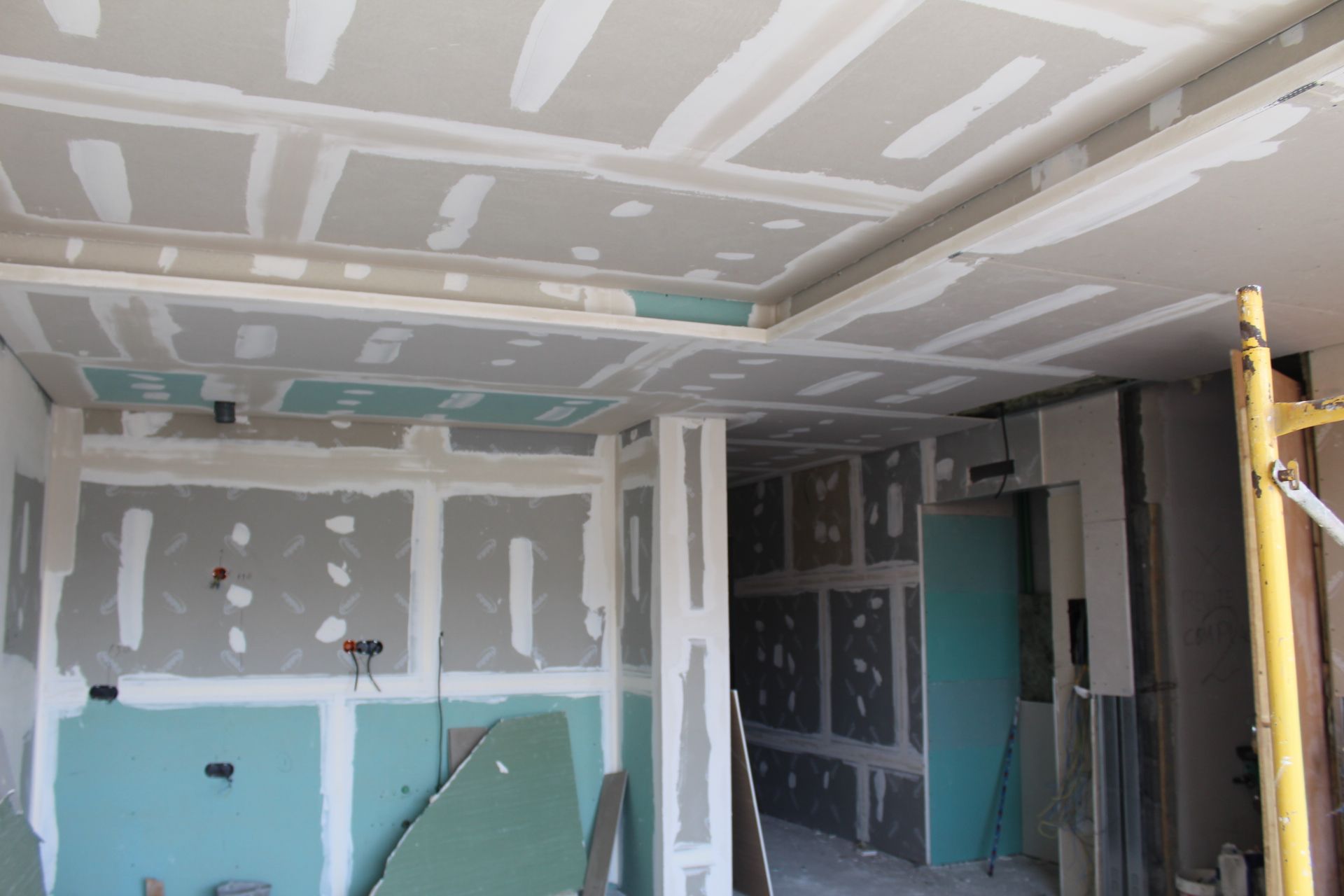 Interior em construção; drywall instalado nas paredes e no teto, sala com superfícies inacabadas.