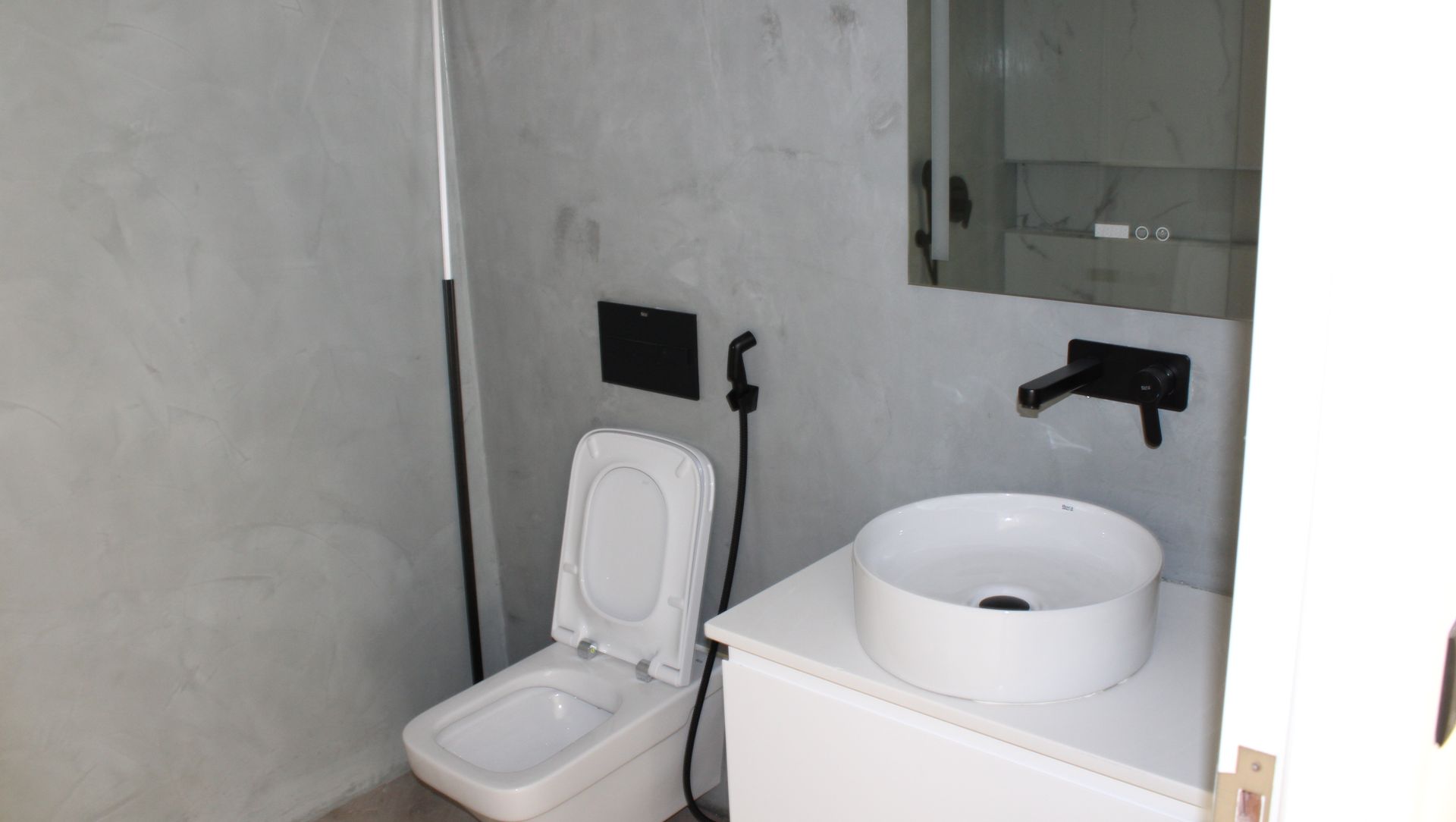 Banheiro com paredes cinzas, vaso sanitário e pia brancos e acessórios pretos.