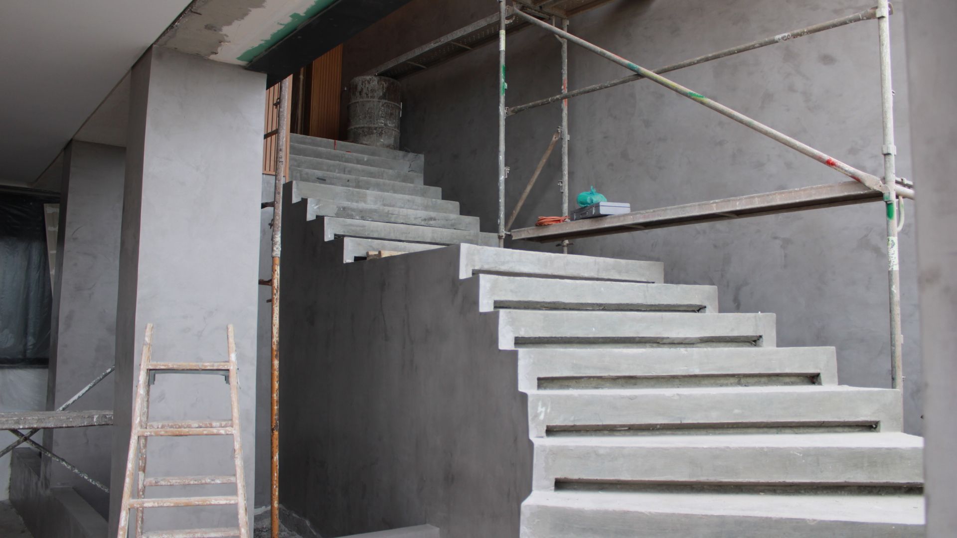 Escada de concreto em construção, cinza com andaimes e ferramentas.