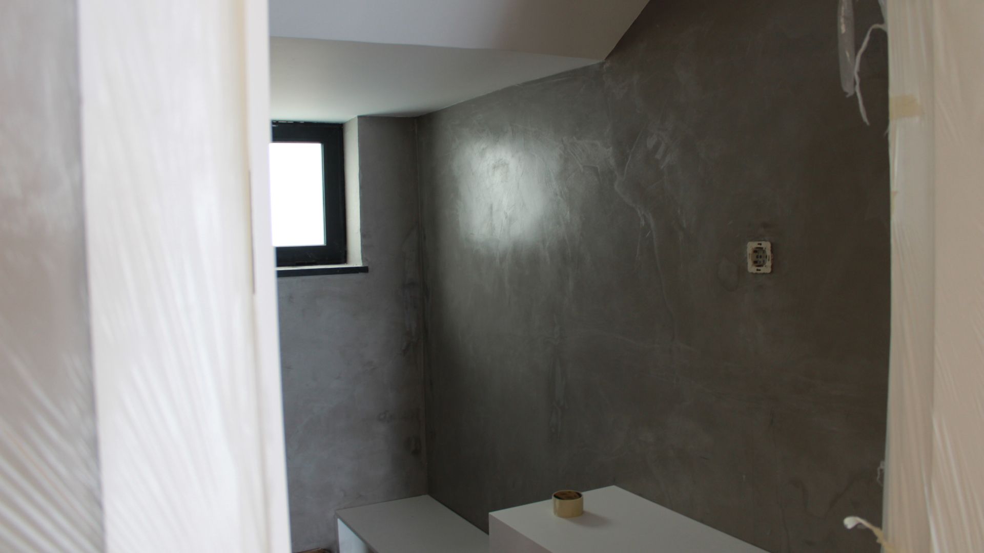 Uma sala cinza com uma pequena janela, detalhes brancos e uma mesa branca; vista da entrada.