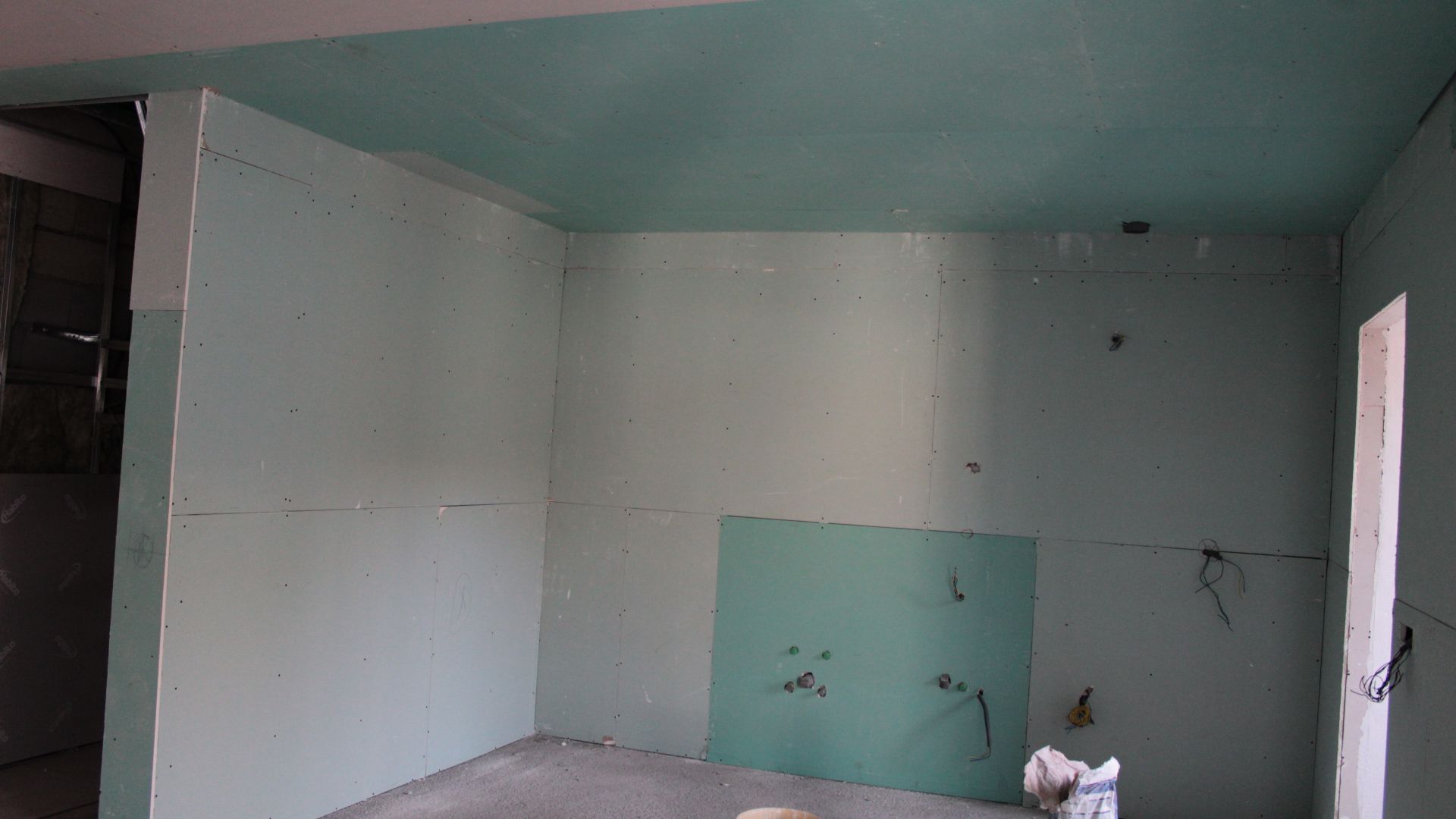 Sala com drywall verde-claro nas paredes e no teto, interior inacabado com uma porta aberta.