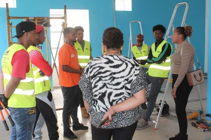 Um grupo de trabalhadores da construção civil está ao redor de uma mulher com uma camisa com estampa de zebra.