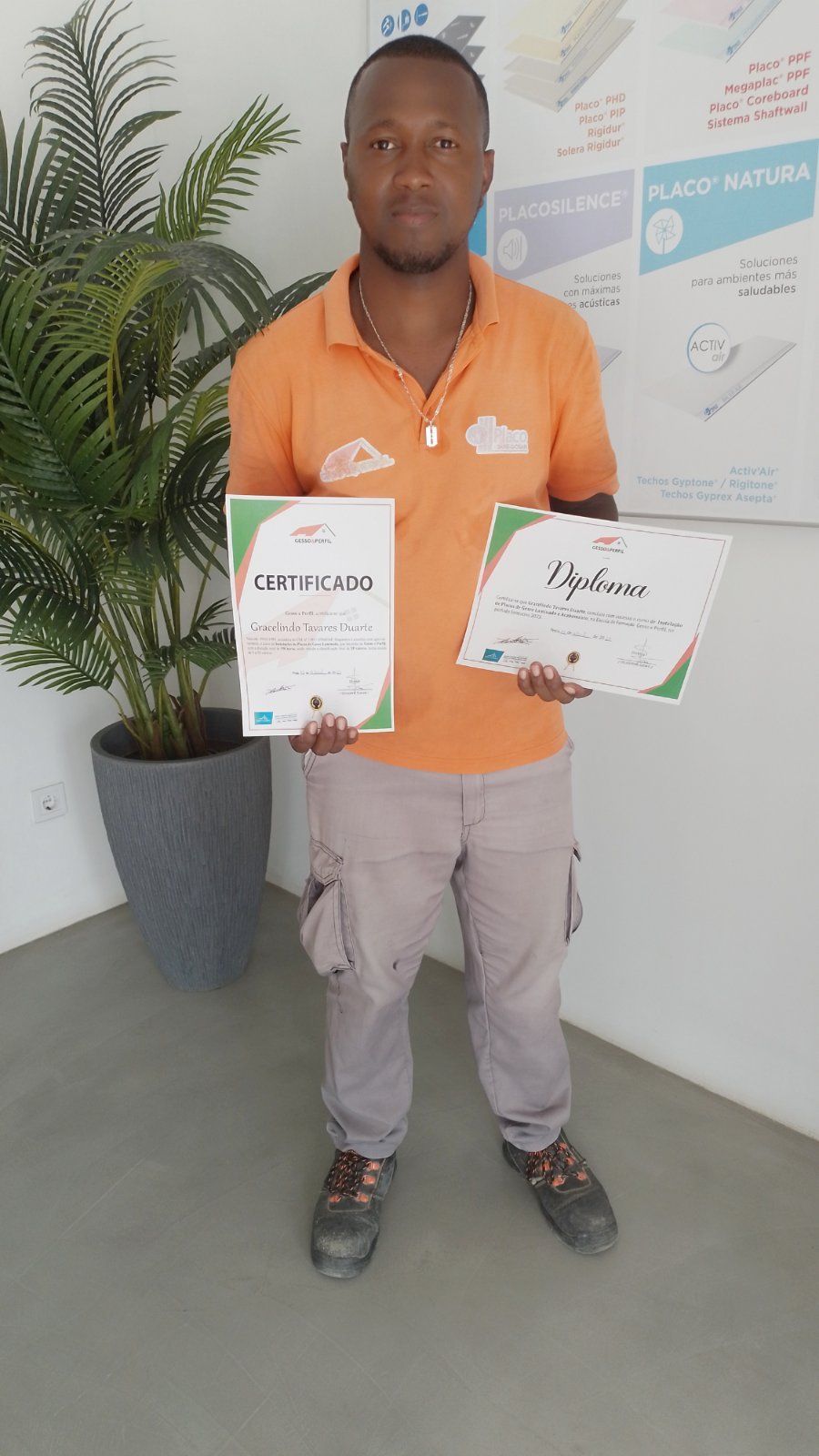Um homem de camisa laranja está segurando dois certificados