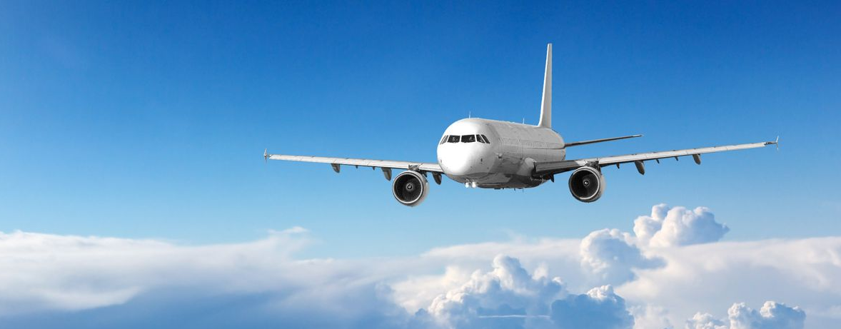 Ein weißes Verkehrsflugzeug fliegt durch einen klaren blauen Himmel über vereinzelten weißen Wolken.