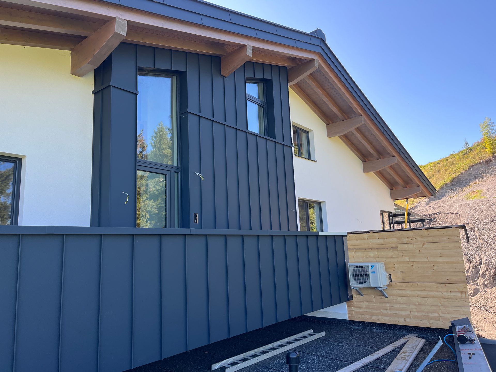 Arbeiter repariert auf einem roten Ziegeldach ein Dachfenster unter klarem, blauem Himmel