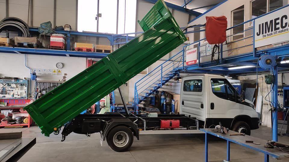 Un camión volquete blanco con una caja verde está estacionado en un garaje.
