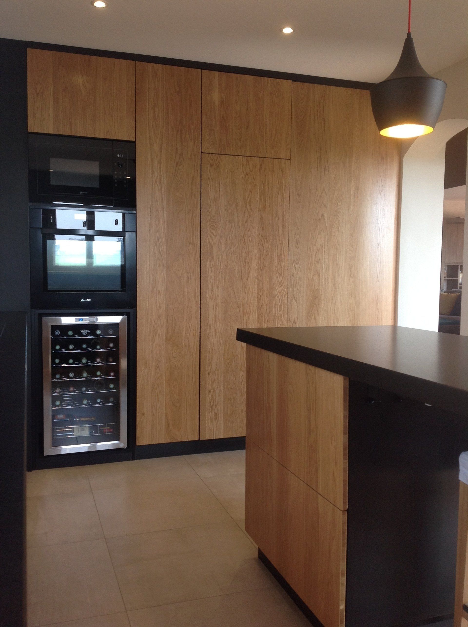 Cuisine revêtement en bois, plan de travail noir, cave à vin et îlot central