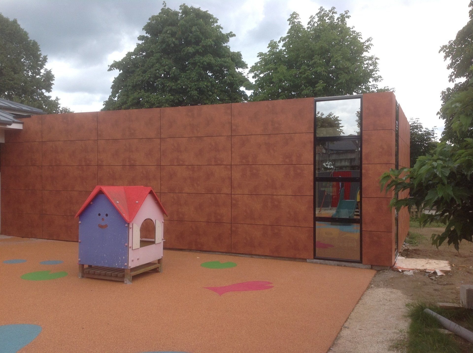 Jardin d'enfant avec cabane en bois et muret avec panneau vitré