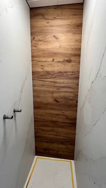 Eine Duschkabine mit Wandpaneelen in Holzoptik, eingefasst von weissen Marmorfliesen und einer Duschwanne mit goldenem Rand.