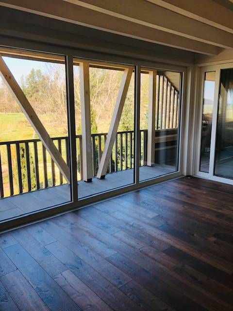 Ein Zimmer mit Holzboden und grossen Glasschiebetüren, die auf einen Balkon mit hölzernen Stützbalken und Geländer führen.