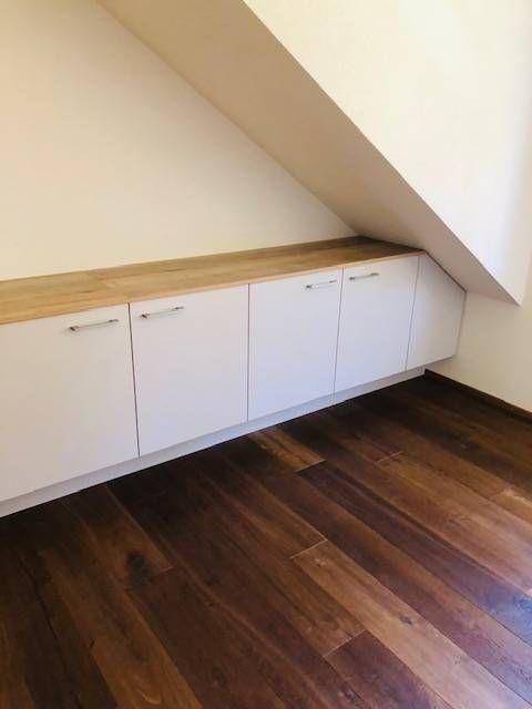 Einbauschränke mit Türen und einer Holzarbeitsplatte, die unter einer Wand über einem dunklen Holzboden angeordnet sind.