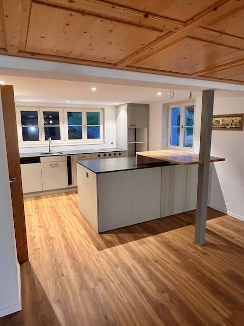 Moderne Küche mit hellgrauen Schränken, einer Kochinsel mit Frühstückstheke aus Holz und holzgetäfelten Decken.