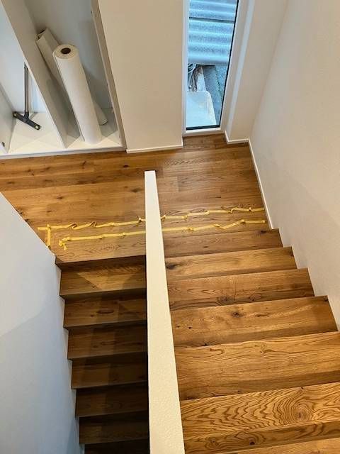 Eine Holztreppe, die von einem Treppenabsatz hinunterblickt, mit einem Handlauf, der Treppenläufe & einen Abstellraum trennt.