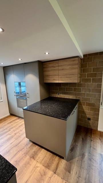 Eine Küche mit einer dunklen Granitinsel, grauen, deckenhohen Schränken, hölzernen Wandschränken und einer Backsteinwand.