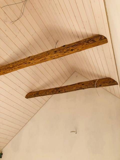 Zwei rustikale Holzbalken an einer weissen, schrägen, holzgetäfelten Decke.