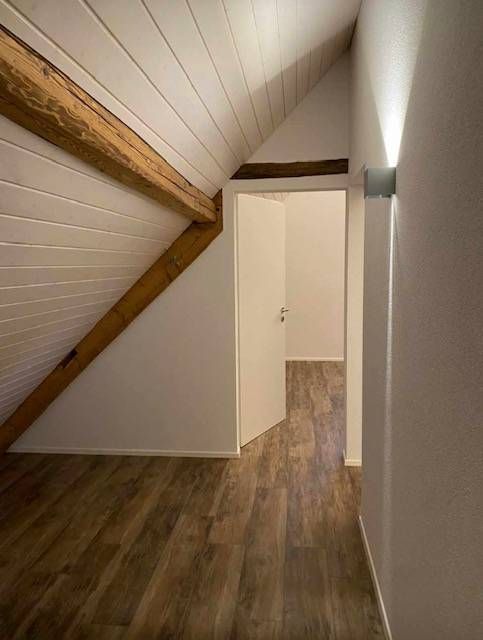 Dachzimmer mit holzgetäfelter Dachschräge, Holzboden und einer weissen Tür, die zu einem angrenzenden Zimmer führt.