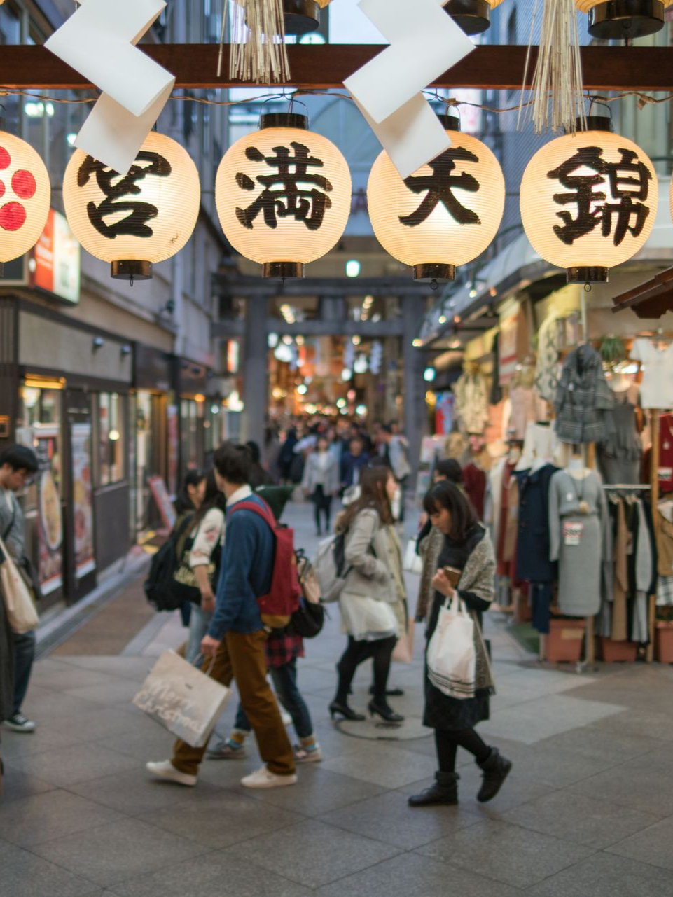 Une rue commerçante japonaise animée avec des lanternes, des passants et des magasins.