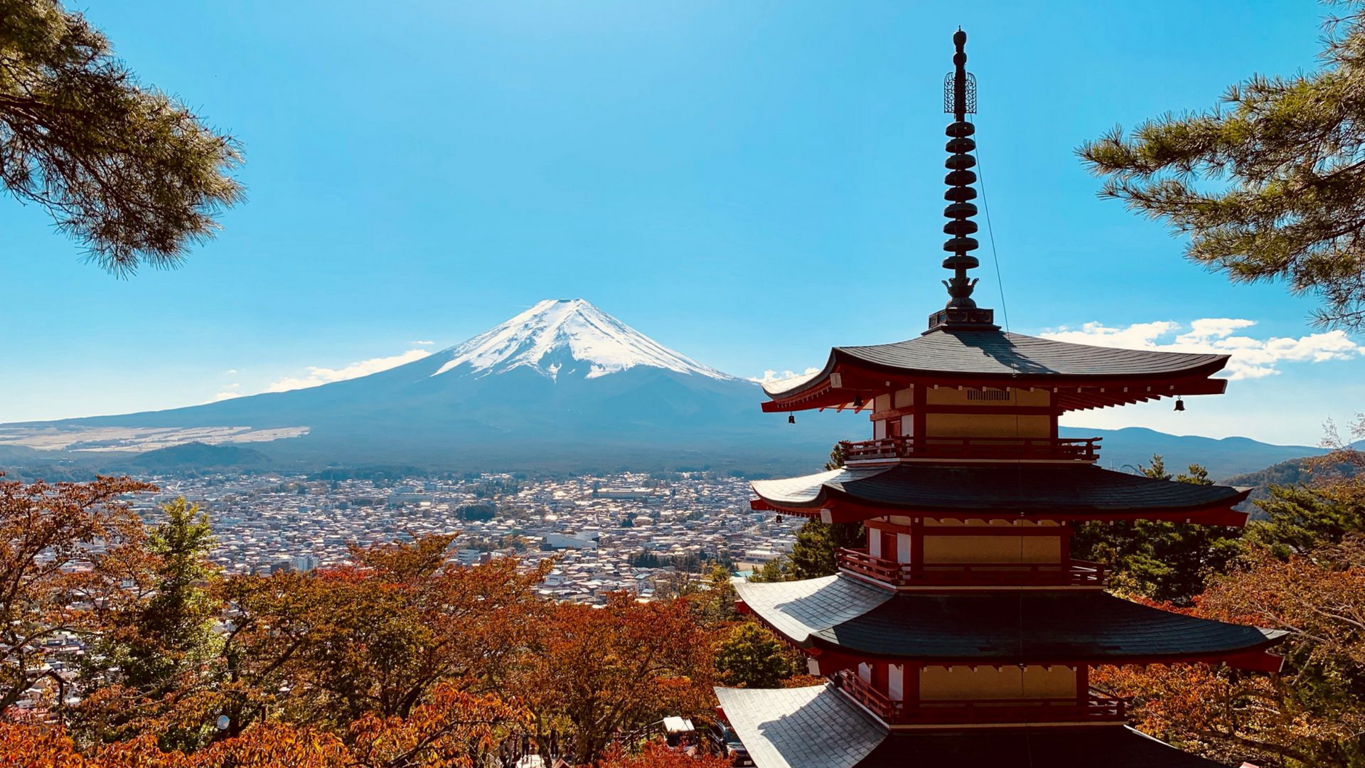 Le Mont Fuji au Japon, vu derrière une pagode, surplombant une ville sous un ciel bleu.