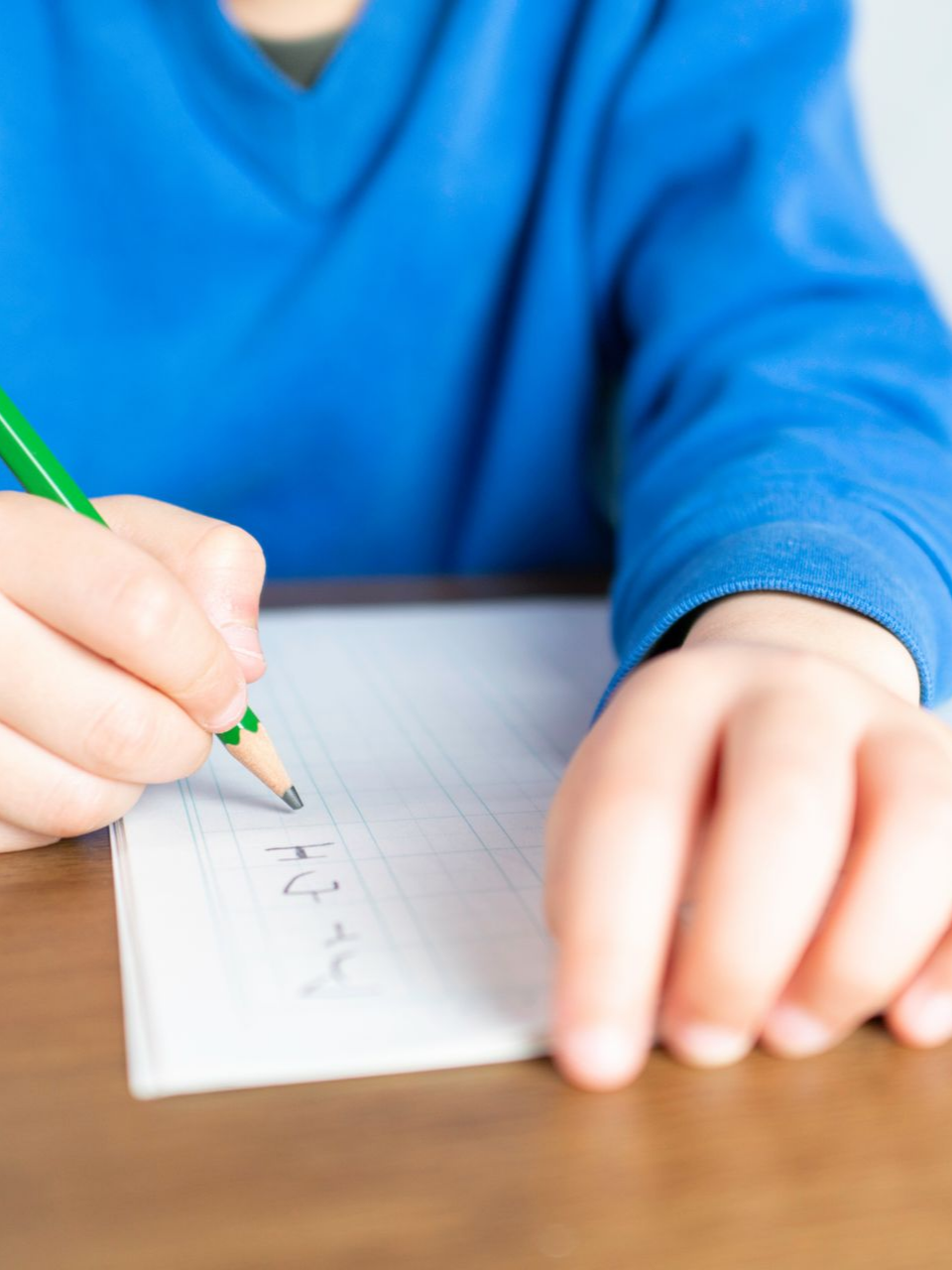 Enfant écrivant sur du papier avec un crayon, portant un pull bleu.
