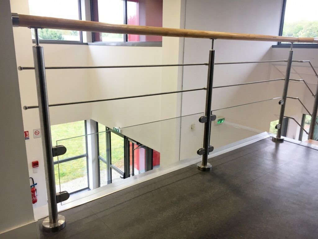 Garde-corps en acier avec des parois vitrées en bas, placé sur un palier avec une ouverture sur le rez-de-chaussée