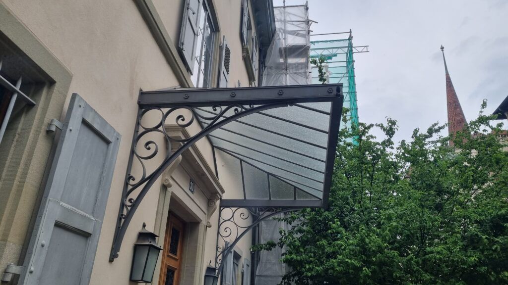 Pose de la marquise en fer forgé avec des vitres opaques au-dessus d'une porte d'entrée