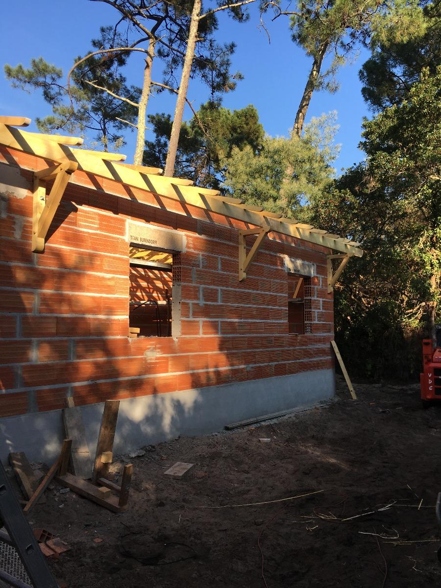 Maison en brique en cours de  construction par beau temps entourée d'arbres