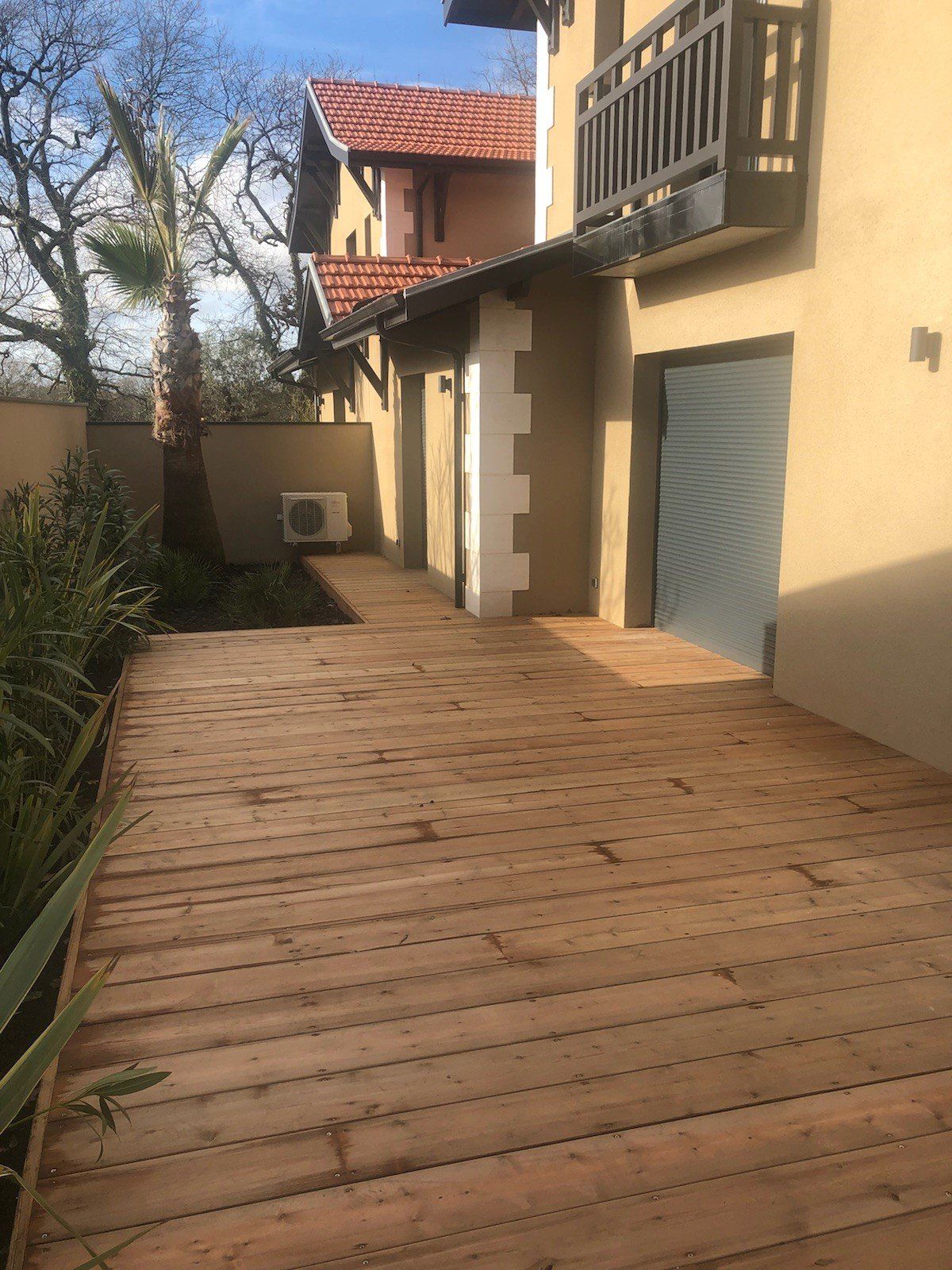 Terrasse bardée en bois devant une façade marron clair