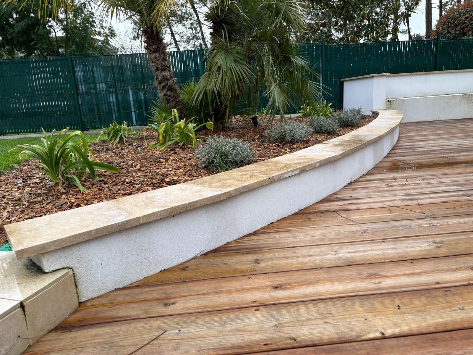Détail d'un jardin aménagé par VD Construction avec un muret blanc au bord d'un plancher en bois